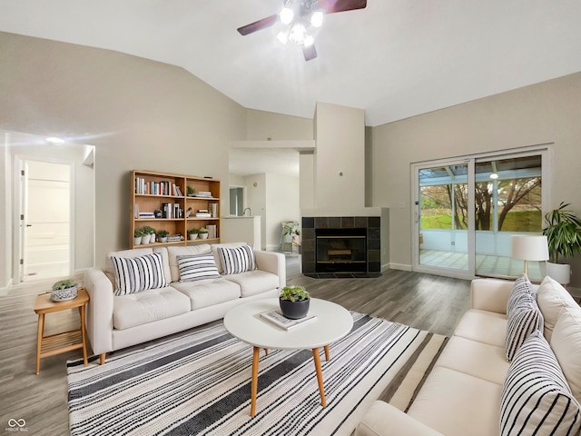 living room with vaulted ceiling, a tiled fireplace, wood finished floors, and a ceiling fan