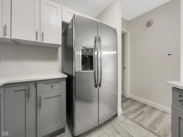 kitchen with light countertops, stainless steel fridge, baseboards, gray cabinetry, and light wood-style flooring