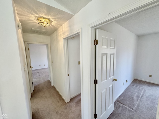 corridor featuring a textured ceiling, baseboards, and light carpet