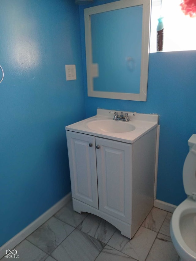 half bathroom with baseboards, marble finish floor, toilet, and vanity