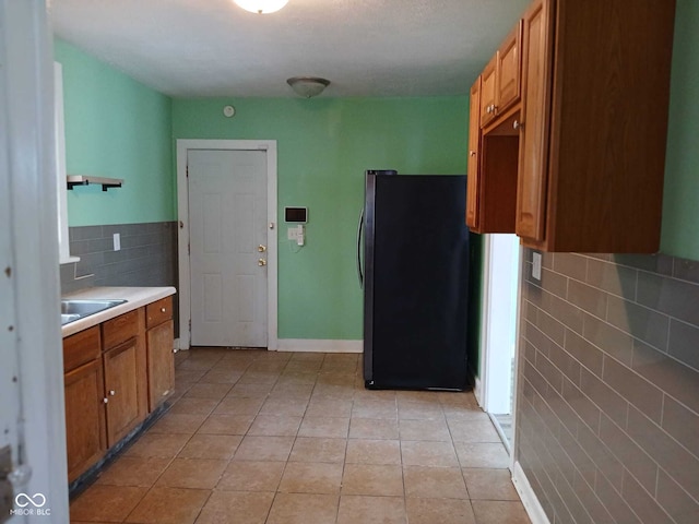 kitchen featuring decorative backsplash, light countertops, brown cabinets, light tile patterned floors, and freestanding refrigerator