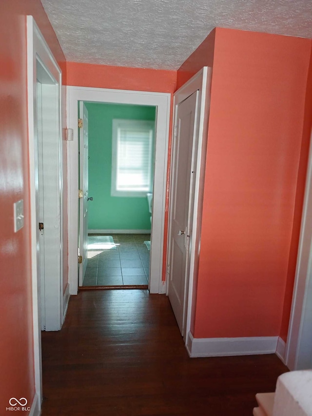 hallway featuring baseboards, a textured ceiling, and wood finished floors