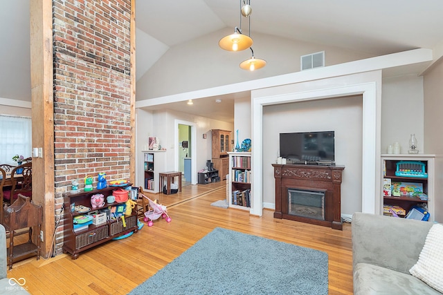living area with a fireplace, wood finished floors, visible vents, and high vaulted ceiling