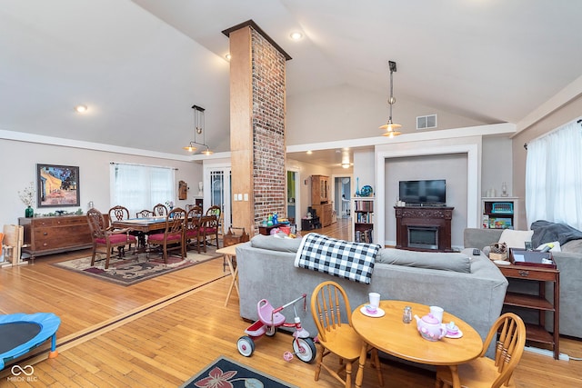 living room with decorative columns, a glass covered fireplace, visible vents, high vaulted ceiling, and wood-type flooring