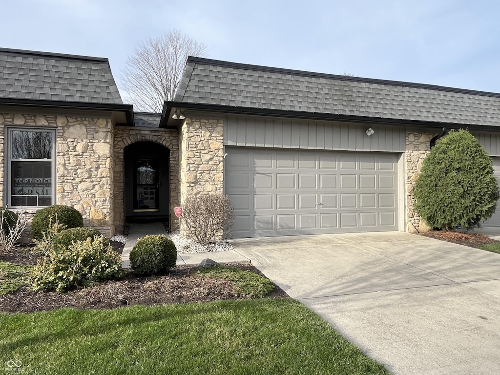 1054 Carters Grv, Indianapolis, IN 46260 - view of front of home featuring a shingled roof, mansard roof, an attached garage, and stone siding