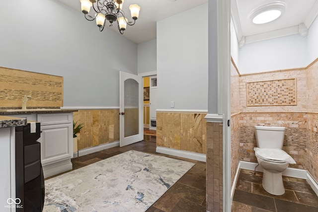 10821 Club Point Dr, Fishers, IN 46037 - full bathroom featuring stone tile floors, wood walls, toilet, a notable chandelier, and wainscoting