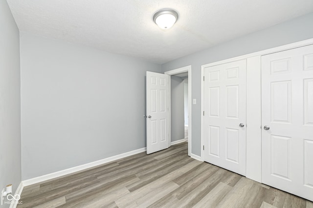 unfurnished bedroom with a closet, baseboards, light wood finished floors, and a textured ceiling