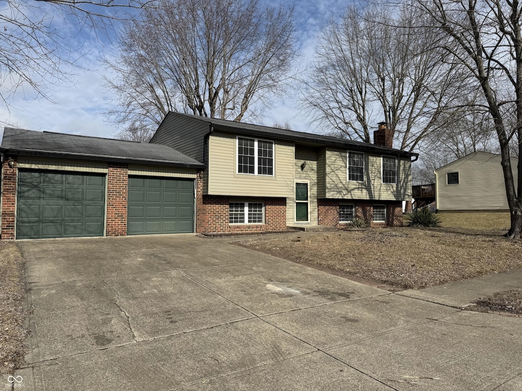 split foyer home featuring brick siding, concrete driveway, a chimney, and a garage