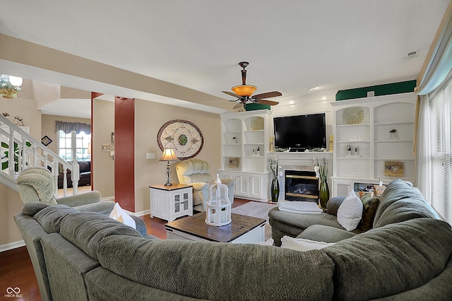 living room with stairs, dark wood-type flooring, visible vents, ceiling fan, and a premium fireplace