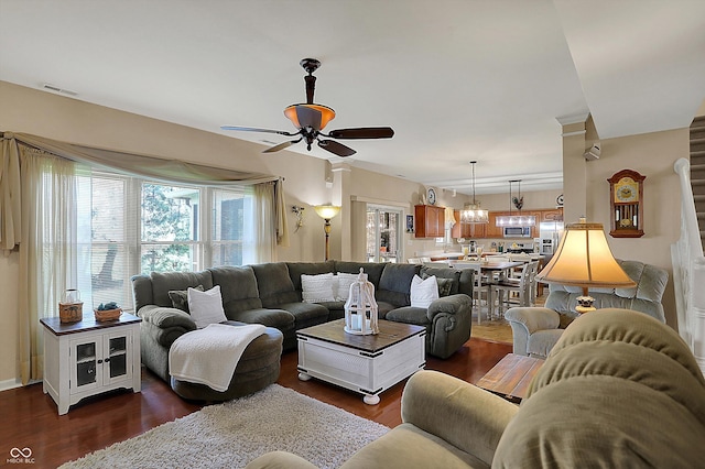 living area featuring dark wood-style flooring, visible vents, and ceiling fan with notable chandelier