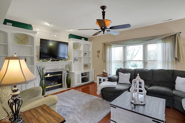 living room featuring dark wood-type flooring, a fireplace with flush hearth, visible vents, and ceiling fan