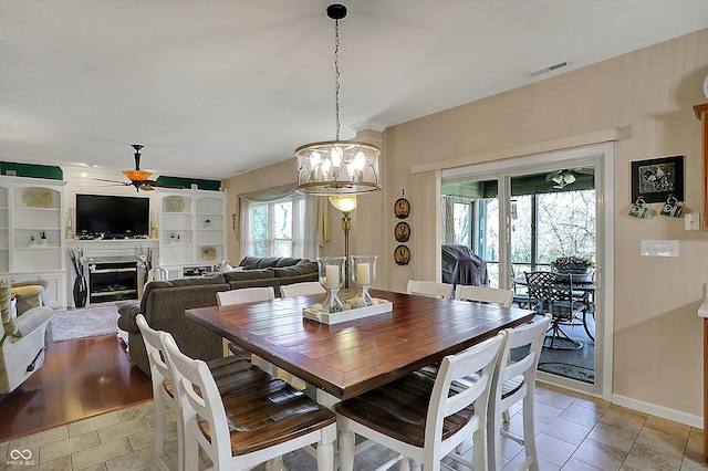 dining area with a glass covered fireplace, baseboards, light tile patterned floors, visible vents, and ceiling fan with notable chandelier