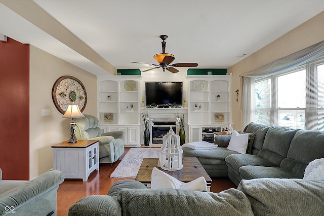 living room featuring dark wood-type flooring, built in features, ceiling fan, and a glass covered fireplace