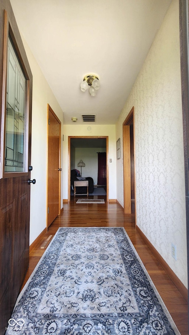 hallway with baseboards, visible vents, and wood finished floors
