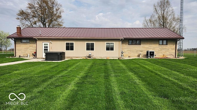 rear view of property featuring metal roof, a yard, a hot tub, stone siding, and a chimney