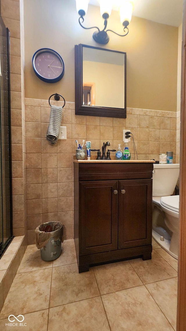 full bath with toilet, tile walls, tile patterned floors, vanity, and wainscoting