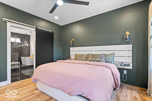 bedroom with a ceiling fan, a barn door, wood finished floors, ensuite bathroom, and recessed lighting