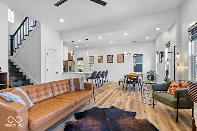 living area featuring a ceiling fan, light wood-style flooring, stairs, and a healthy amount of sunlight