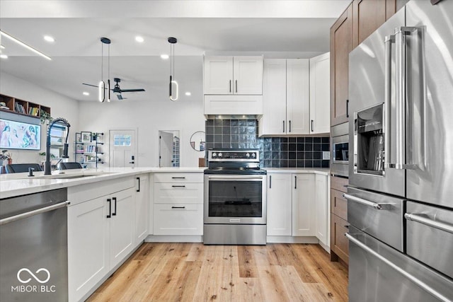 kitchen with white cabinetry, tasteful backsplash, a sink, light wood finished floors, and stainless steel appliances