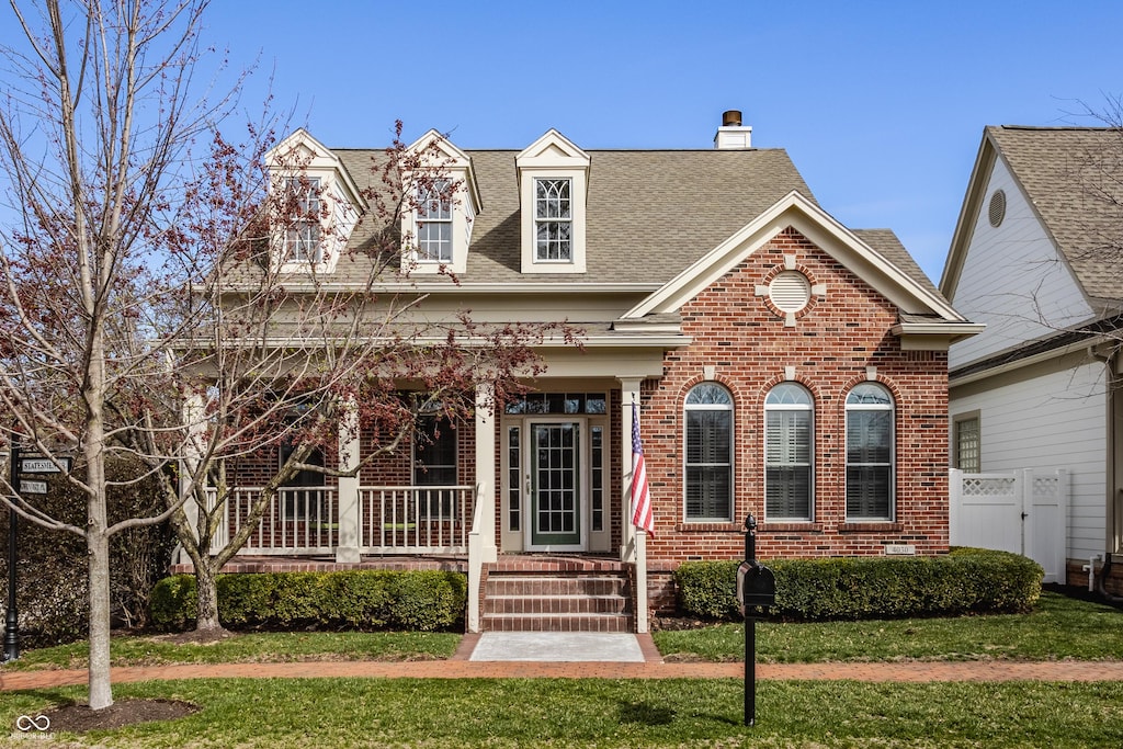 4030 Statesmen Dr, Indianapolis, IN 46250 - view of front of house featuring roof with shingles, a front yard, brick siding, a porch, and a chimney