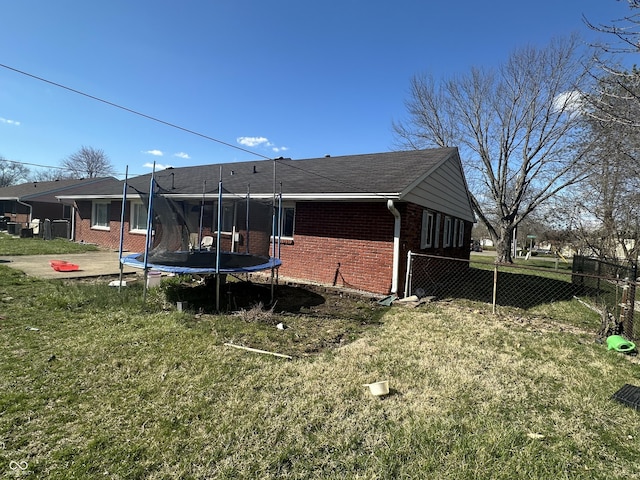 back of house with a yard, a trampoline, and brick siding