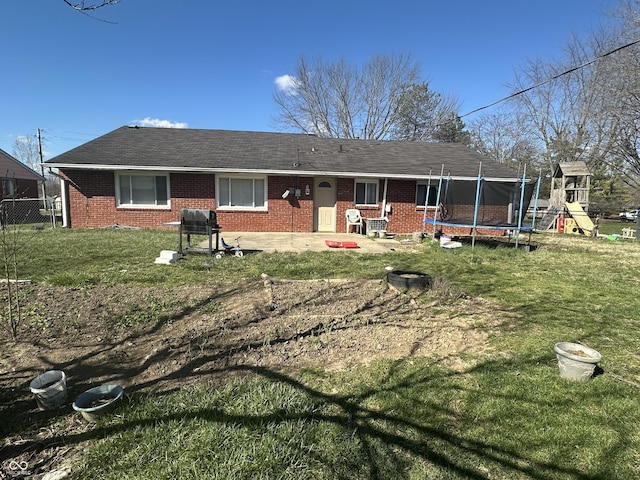 rear view of property with a playground, a trampoline, a lawn, and brick siding