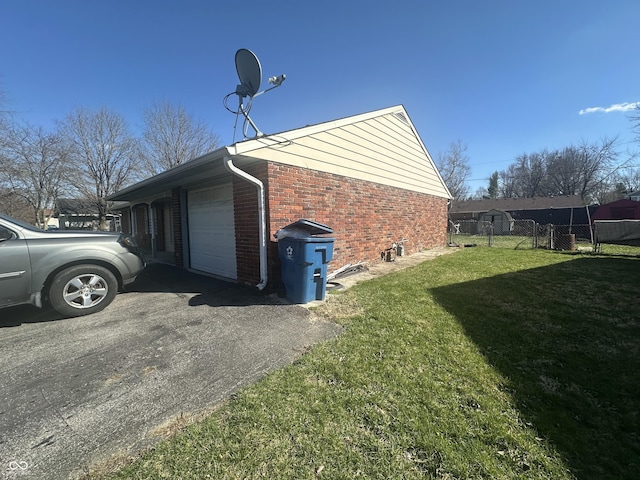 view of side of home featuring brick siding, fence, aphalt driveway, a lawn, and a garage