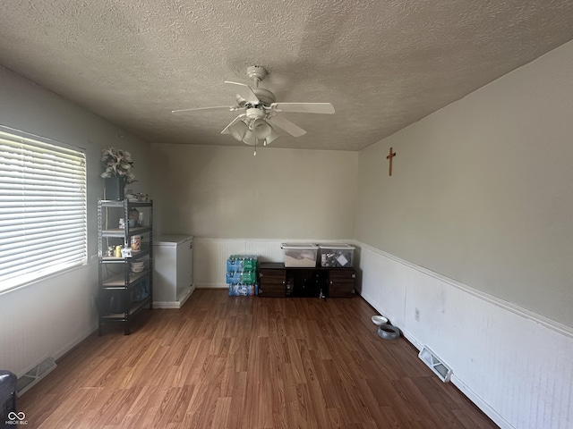 unfurnished office featuring a textured ceiling, a ceiling fan, wood finished floors, visible vents, and wainscoting
