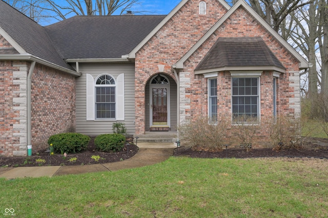 view of front of home with brick siding, a shingled roof, and a front lawn