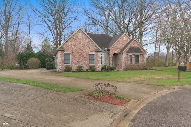 view of front of home with brick siding, curved driveway, and a front yard