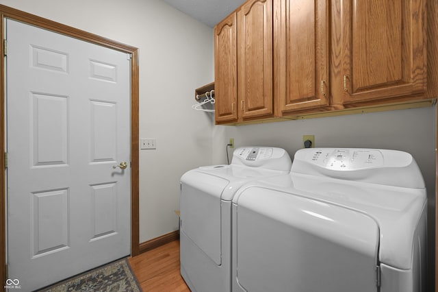clothes washing area featuring baseboards, cabinet space, light wood-type flooring, and washer and dryer