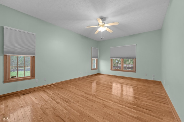 spare room with a wealth of natural light, visible vents, a ceiling fan, and wood finished floors