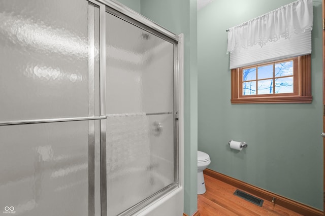 full bathroom with toilet, wood finished floors, baseboards, visible vents, and shower / bath combination with glass door
