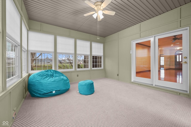 unfurnished sunroom featuring carpet flooring, ceiling fan, and a decorative wall