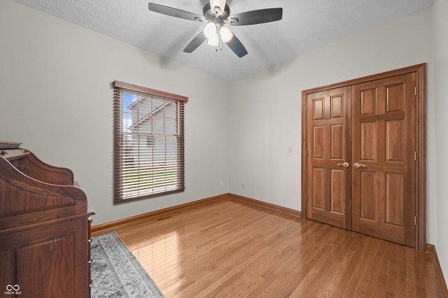 bedroom with baseboards, light wood-type flooring, a textured ceiling, and a ceiling fan