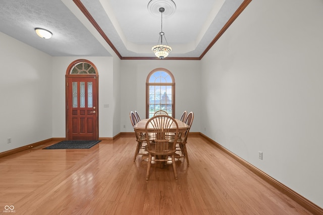 dining room featuring baseboards, a textured ceiling, light wood-type flooring, and a raised ceiling