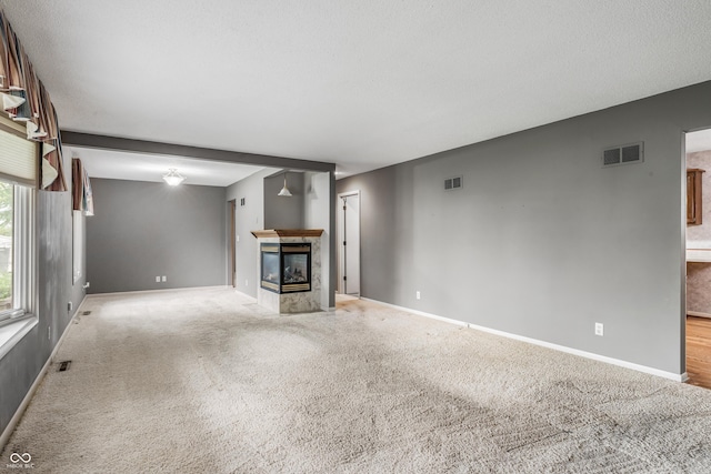 unfurnished living room with a tiled fireplace, baseboards, and light colored carpet