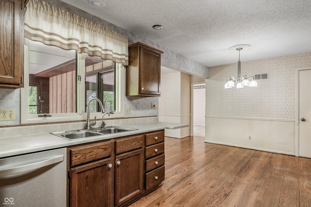 kitchen with dishwasher, a sink, wallpapered walls, light wood-style floors, and wainscoting