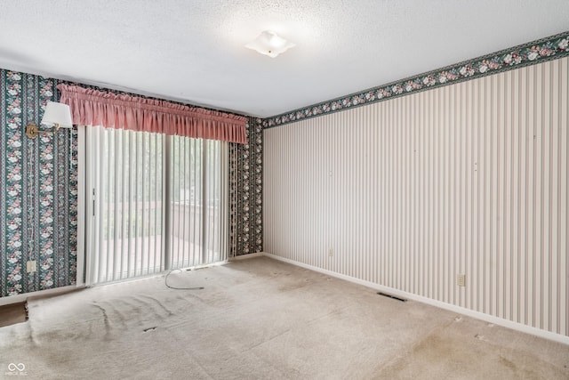 carpeted spare room featuring wallpapered walls, a textured ceiling, and baseboards