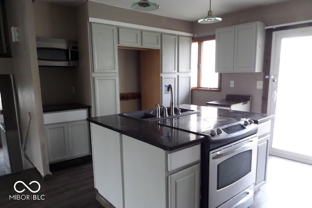 kitchen with an island with sink, a sink, dark countertops, stainless steel appliances, and pendant lighting