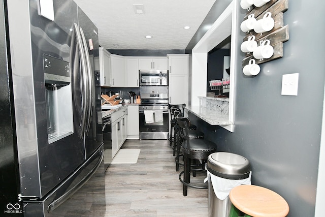 3041 S Kercheval St, Indianapolis, IN 46239 - kitchen featuring light stone counters, light wood finished floors, a kitchen breakfast bar, stainless steel appliances, and white cabinets