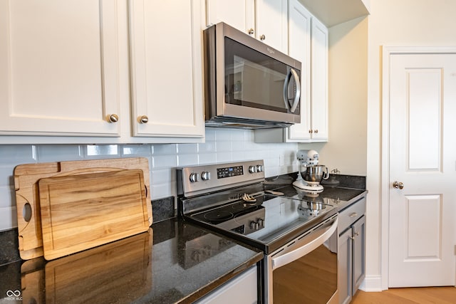 kitchen with light wood finished floors, white cabinetry, appliances with stainless steel finishes, and dark stone counters