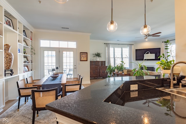 kitchen featuring ornamental molding, dark stone counters, ceiling fan, visible vents, and a fireplace