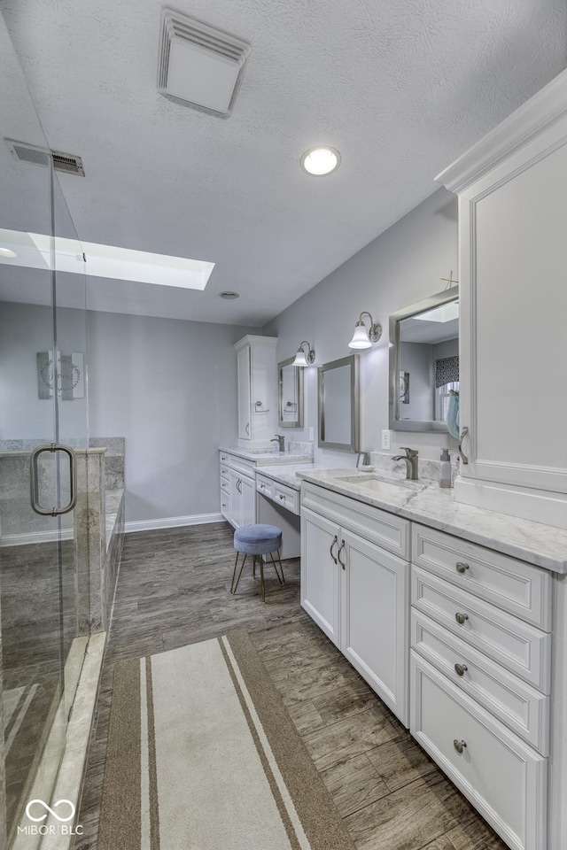 full bath featuring a stall shower, a sink, a skylight, visible vents, and double vanity
