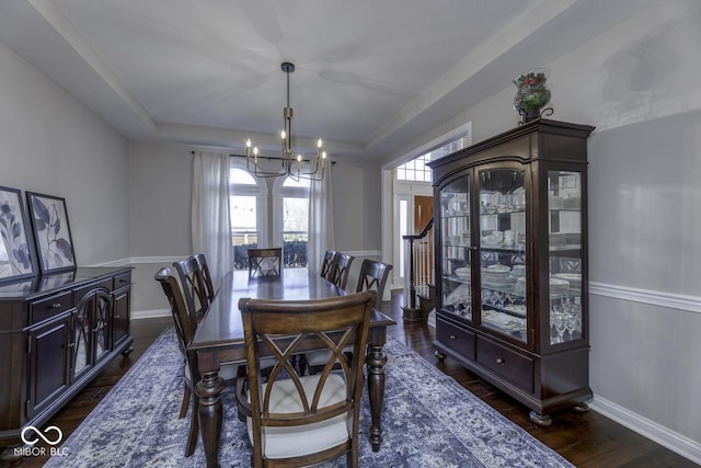 dining space featuring dark wood-type flooring, a tray ceiling, baseboards, and a notable chandelier