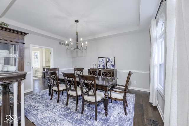dining room with dark wood-type flooring, a tray ceiling, visible vents, and an inviting chandelier