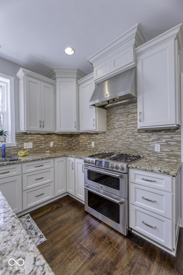 kitchen with range with two ovens, dark wood-style flooring, under cabinet range hood, backsplash, and white cabinets