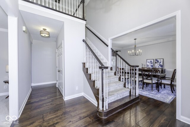 staircase with an inviting chandelier, baseboards, a high ceiling, and wood finished floors
