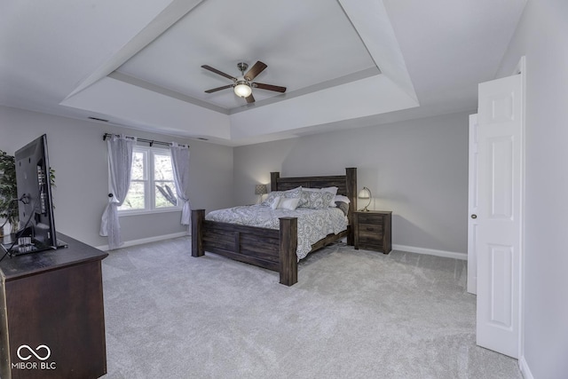 carpeted bedroom with baseboards, a tray ceiling, and a ceiling fan