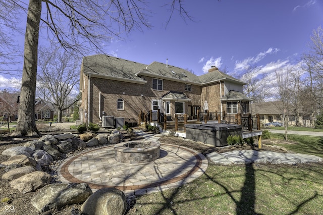 rear view of property featuring a wooden deck, an outdoor fire pit, brick siding, central AC, and a chimney